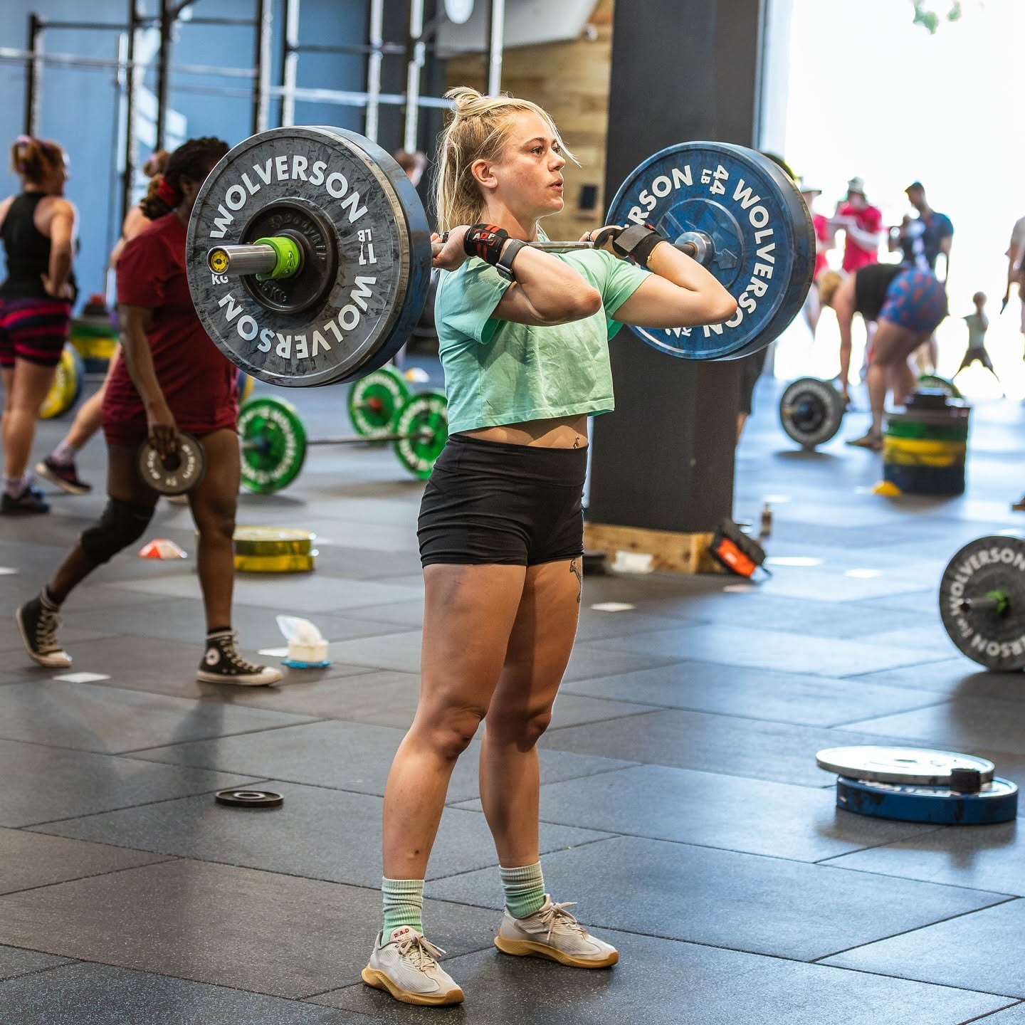 A member front-racking a barbell during a sunlit open-gym session