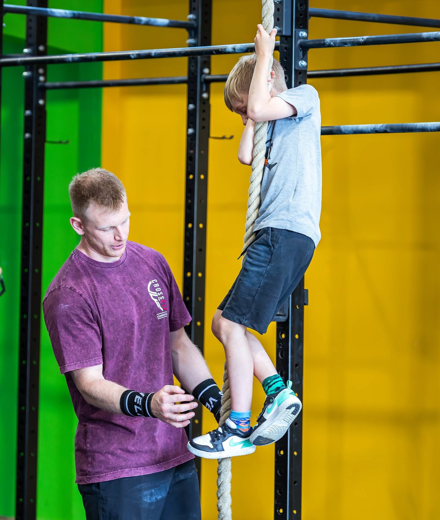 A coach guiding a young boy's feet during a rope climb
