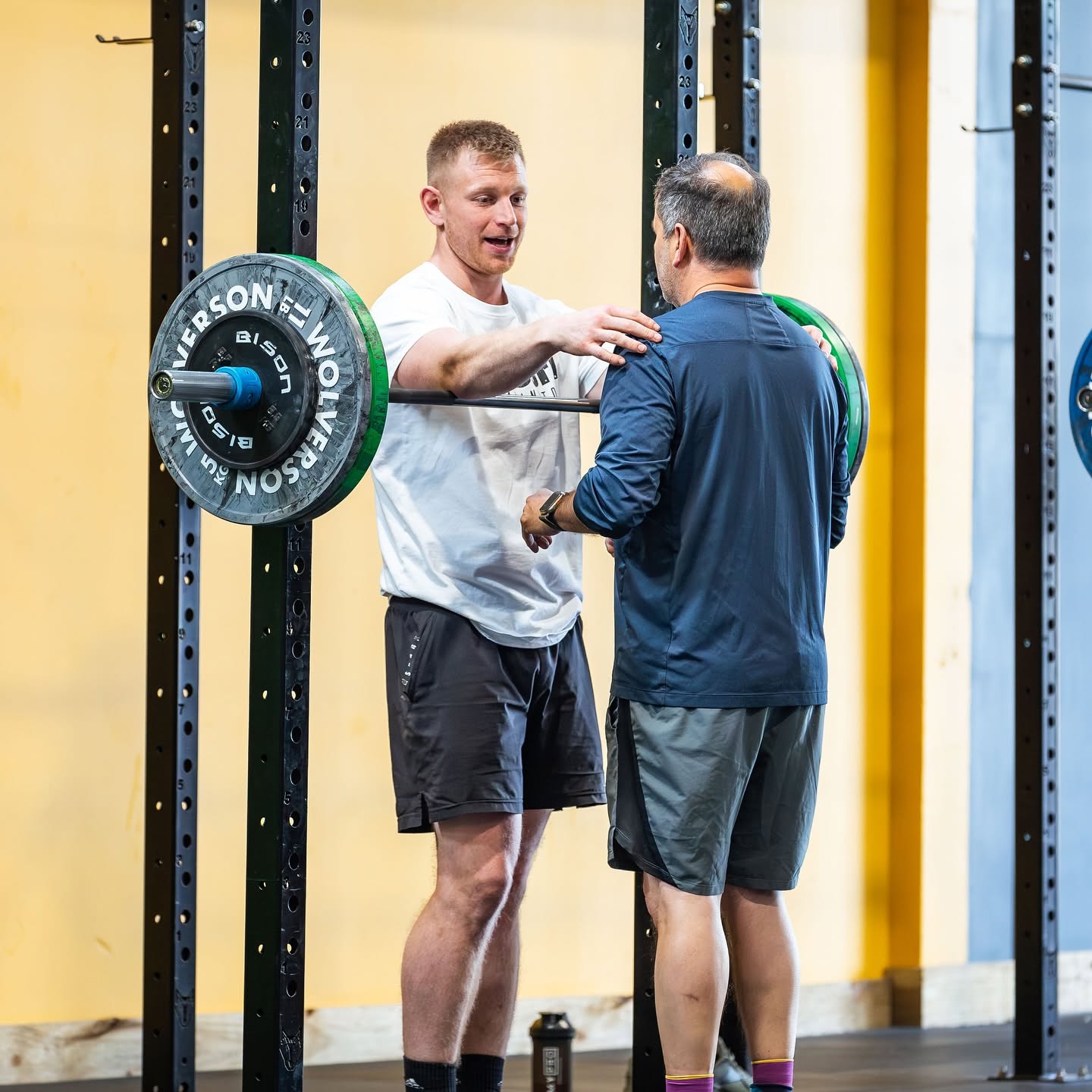 A CrossFit Leamington coach giving hands-on squat coaching at the rack