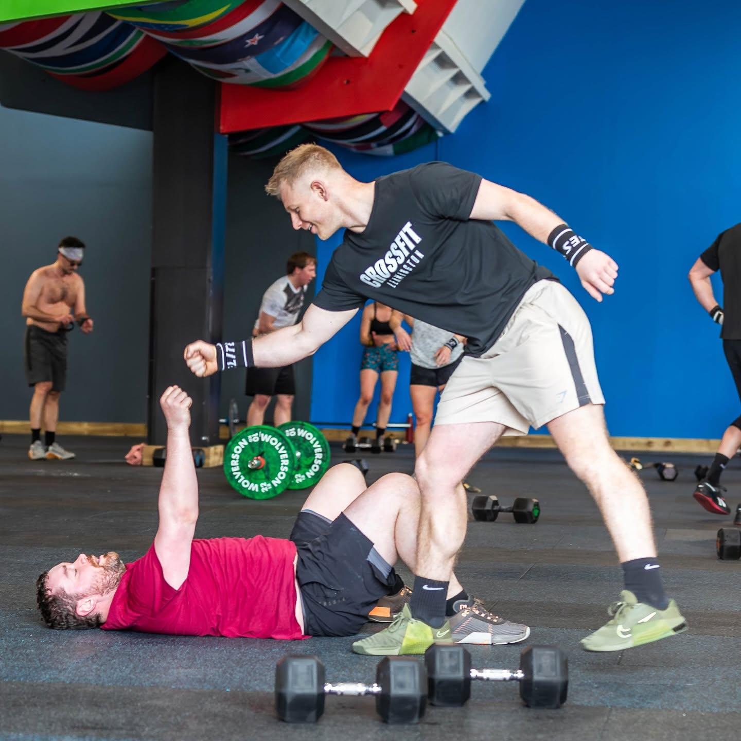 Two members celebrating mid-workout, one fist-pumping beside the dumbbells