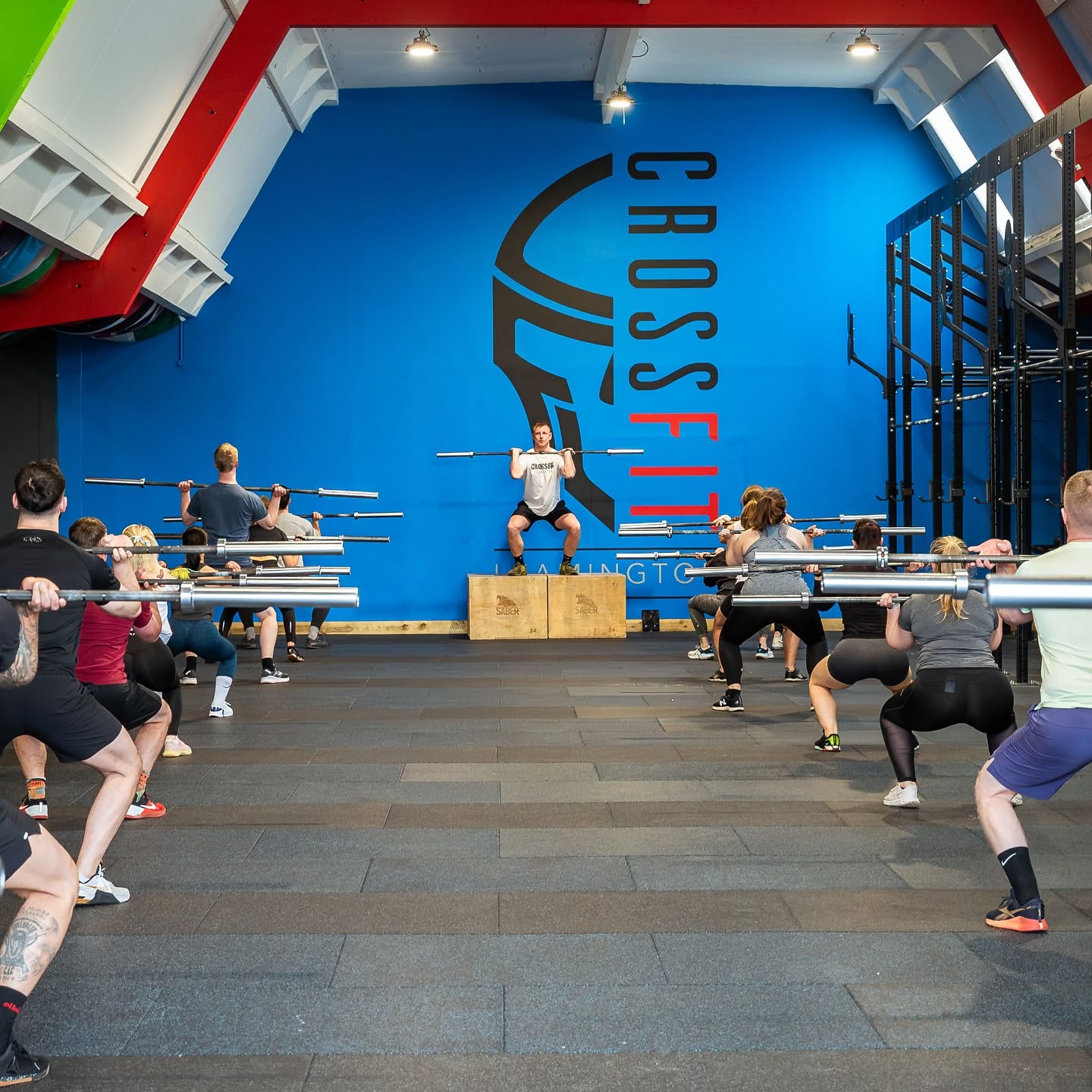A full class at CrossFit Leamington squatting empty barbells together while a coach demonstrates