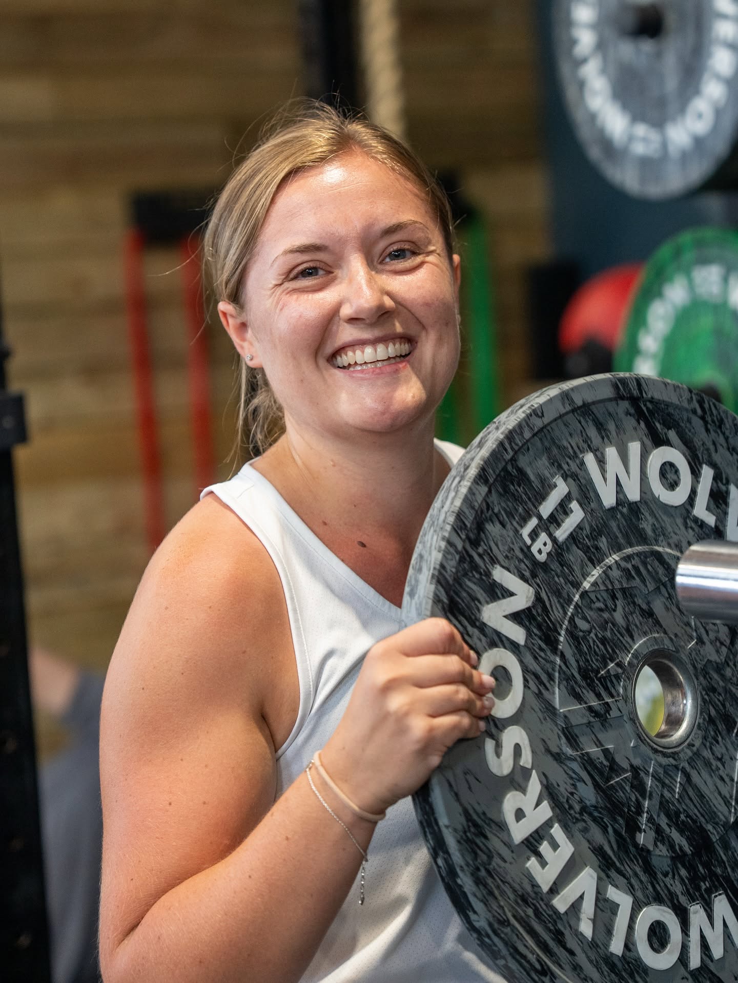 A smiling member carrying a bumper plate to her barbell at CrossFit Leamington