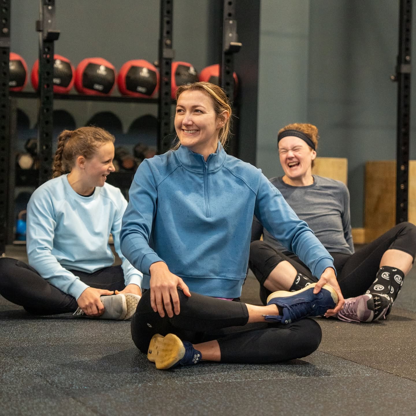 Three CrossFit Leamington members laughing together while stretching after class